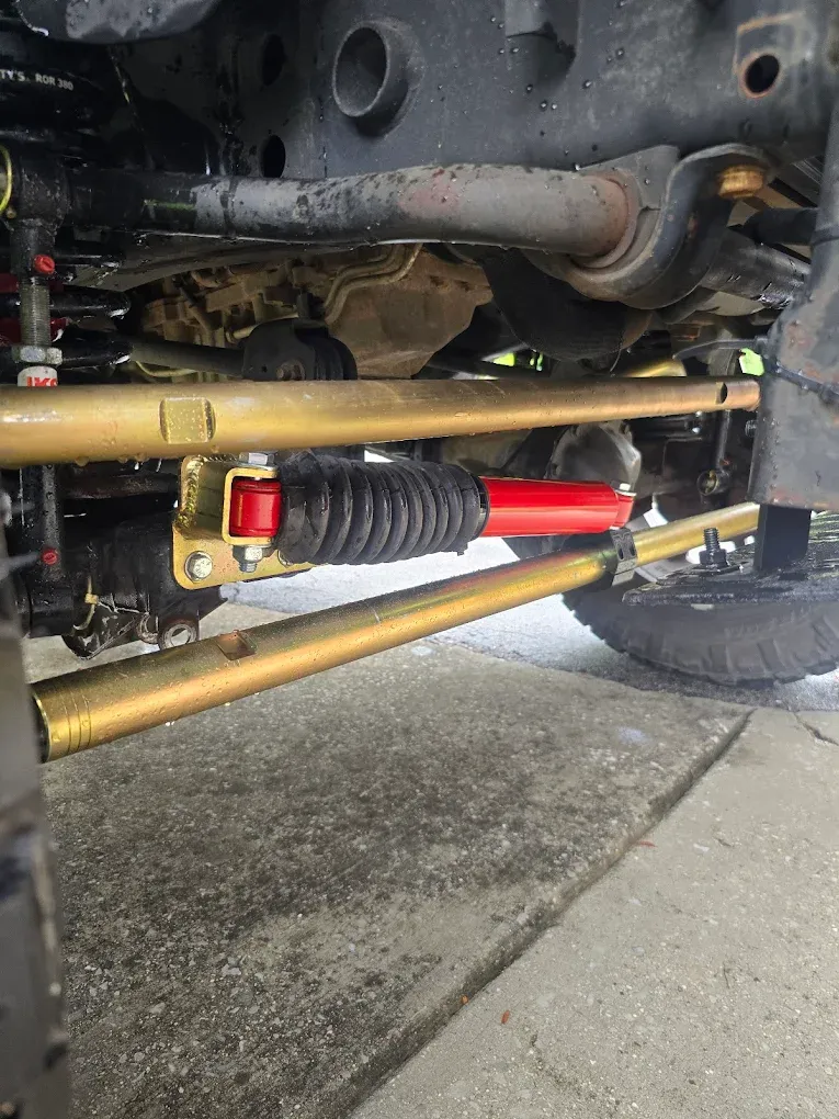 Rear undercarriage of a vehicle showing suspension parts, axle, and a red shock absorber near the wheel.