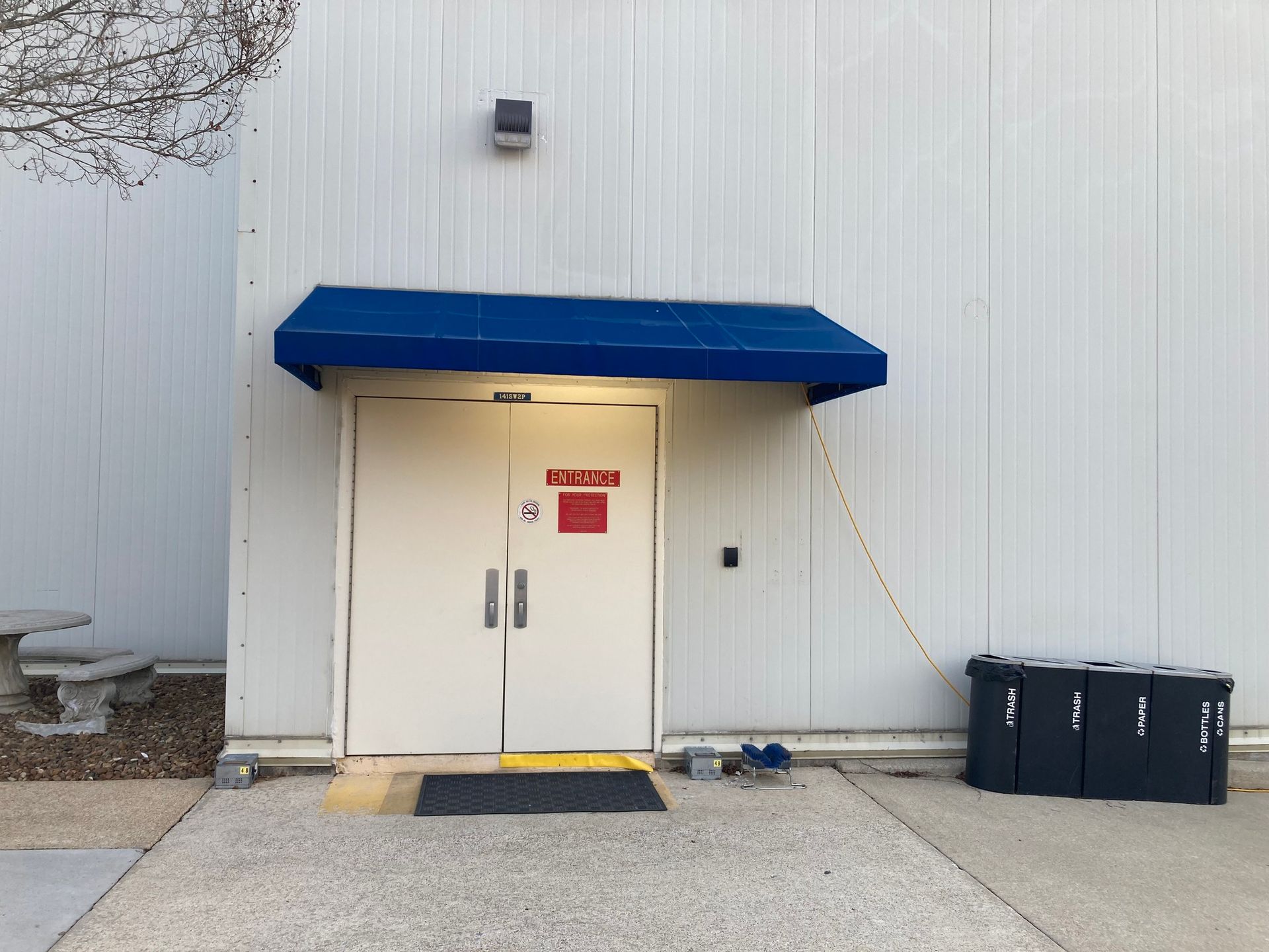 White building entrance with blue awning, double doors, and black equipment cases.