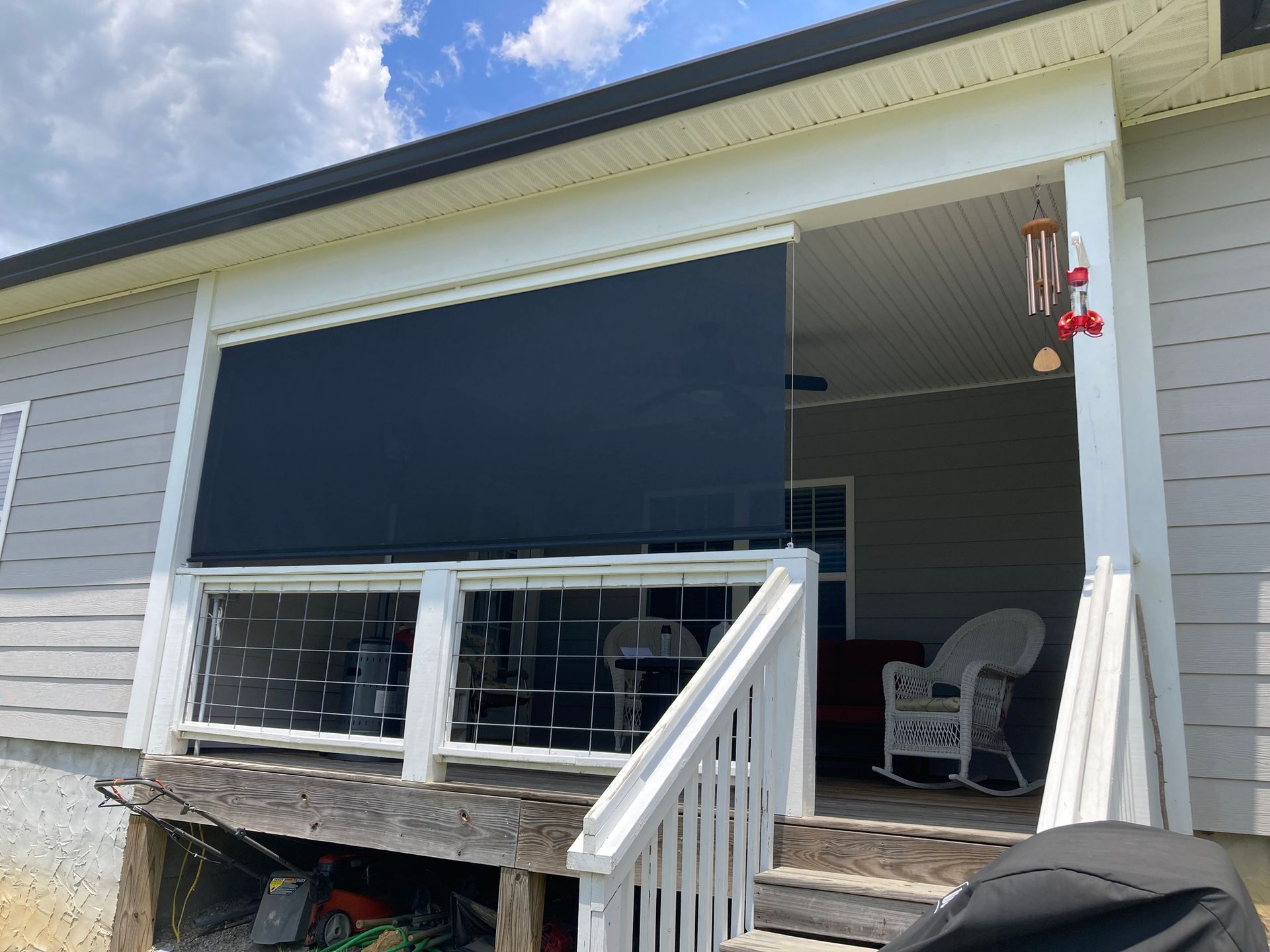 Black shade covers porch opening, white railing and supports, gray siding, sky.