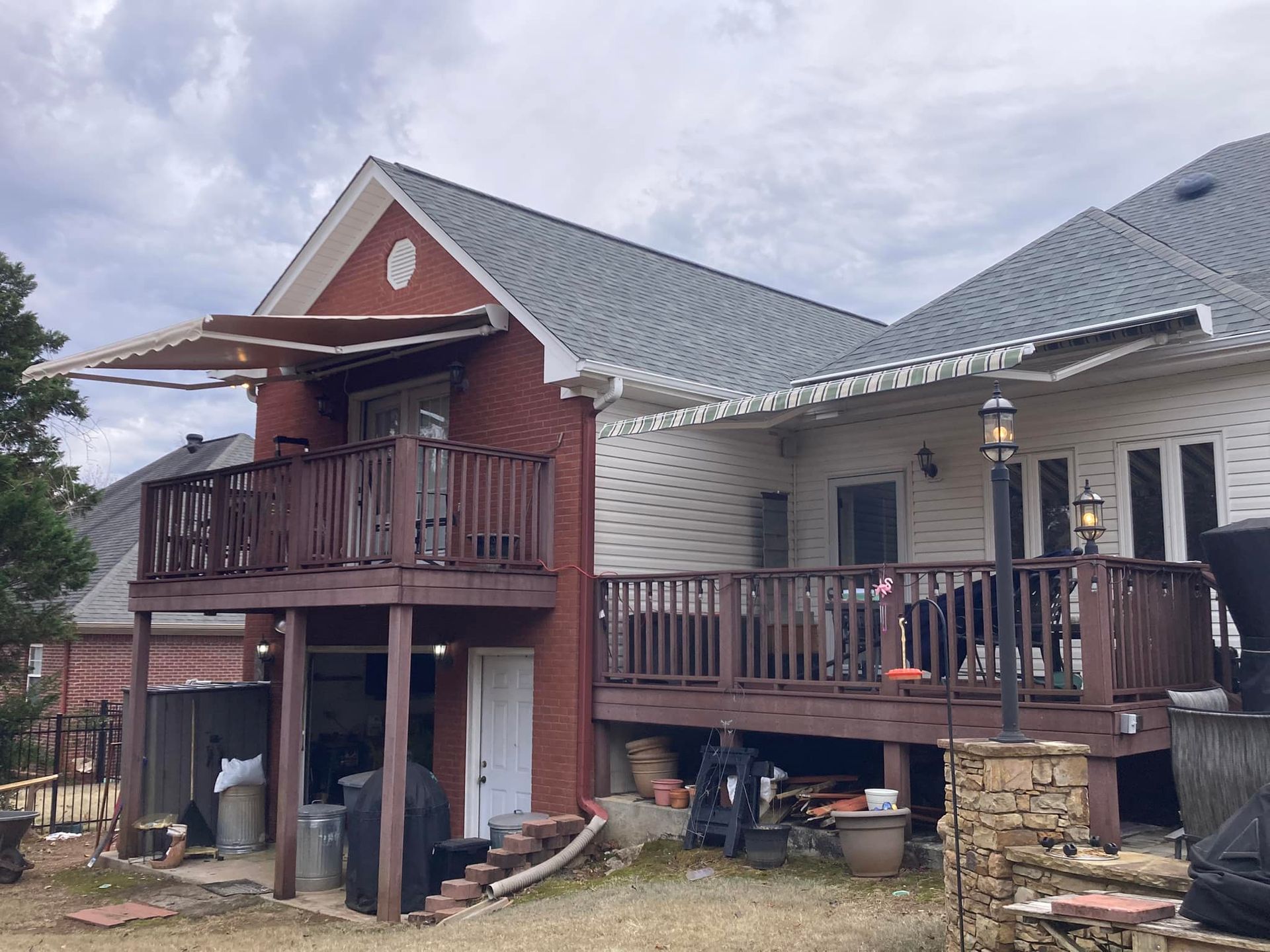 Two-story house with decks; brick and white siding. Awning over a deck, wooden railings, and overcast sky.