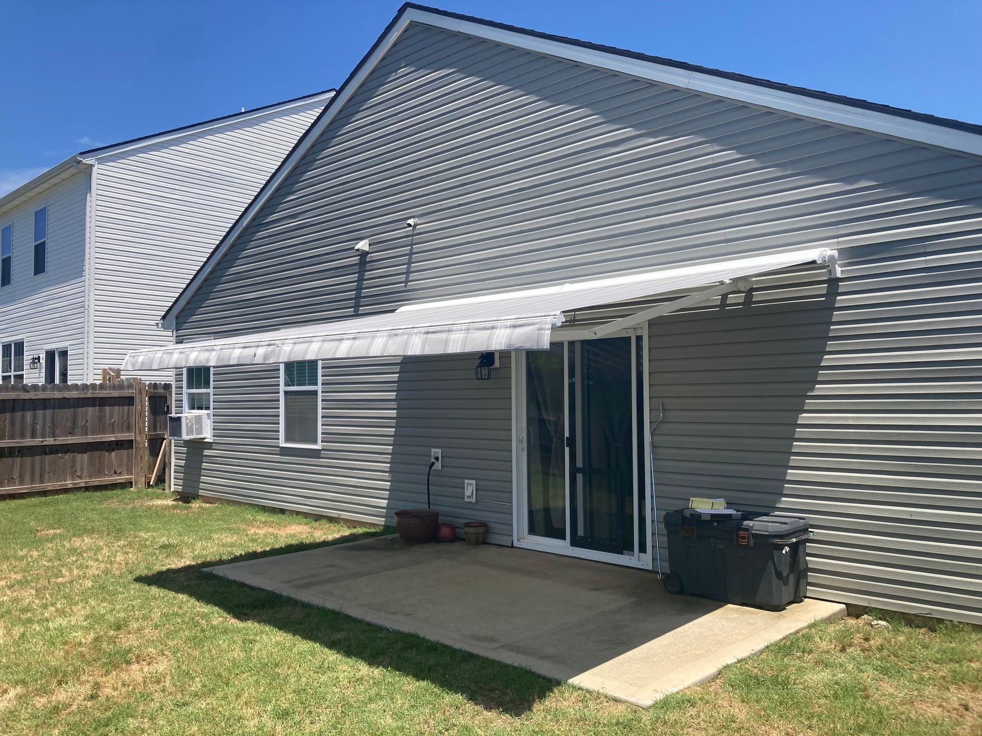 Backyard of a house with gray siding, awning over a sliding glass door, and a concrete patio.