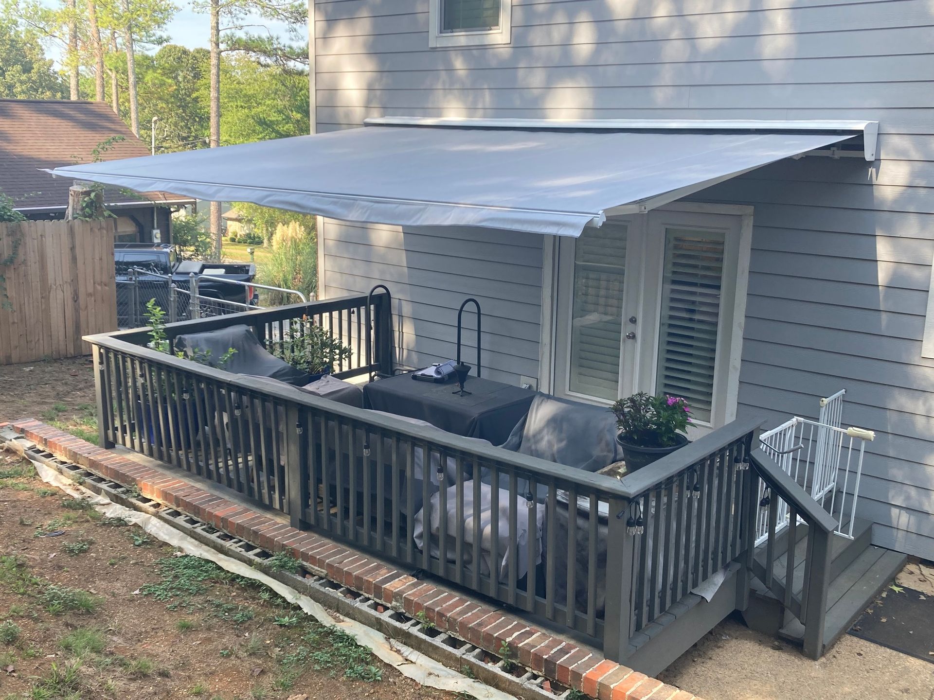 Grey deck with retractable awning, patio furniture, and access to a house.