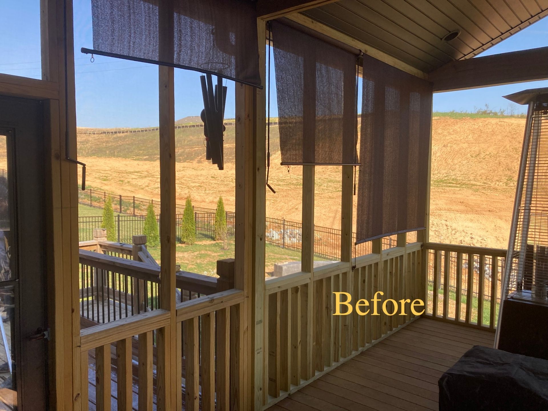 A wooden porch with shades lowered, overlooking a sunny, grassy hillside, labeled 