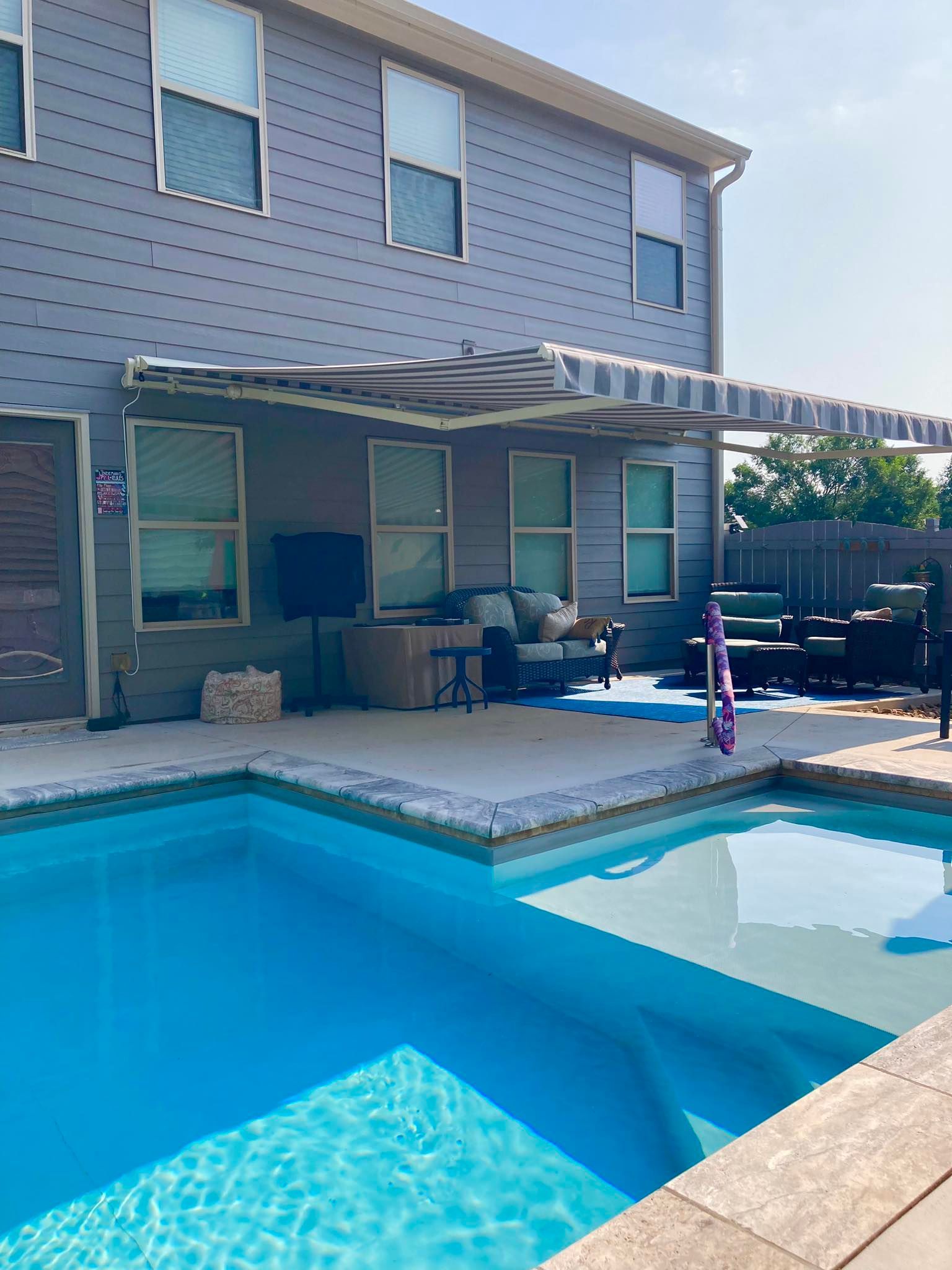 Backyard with pool, patio, and awning; blue and gray color scheme; sunny day.