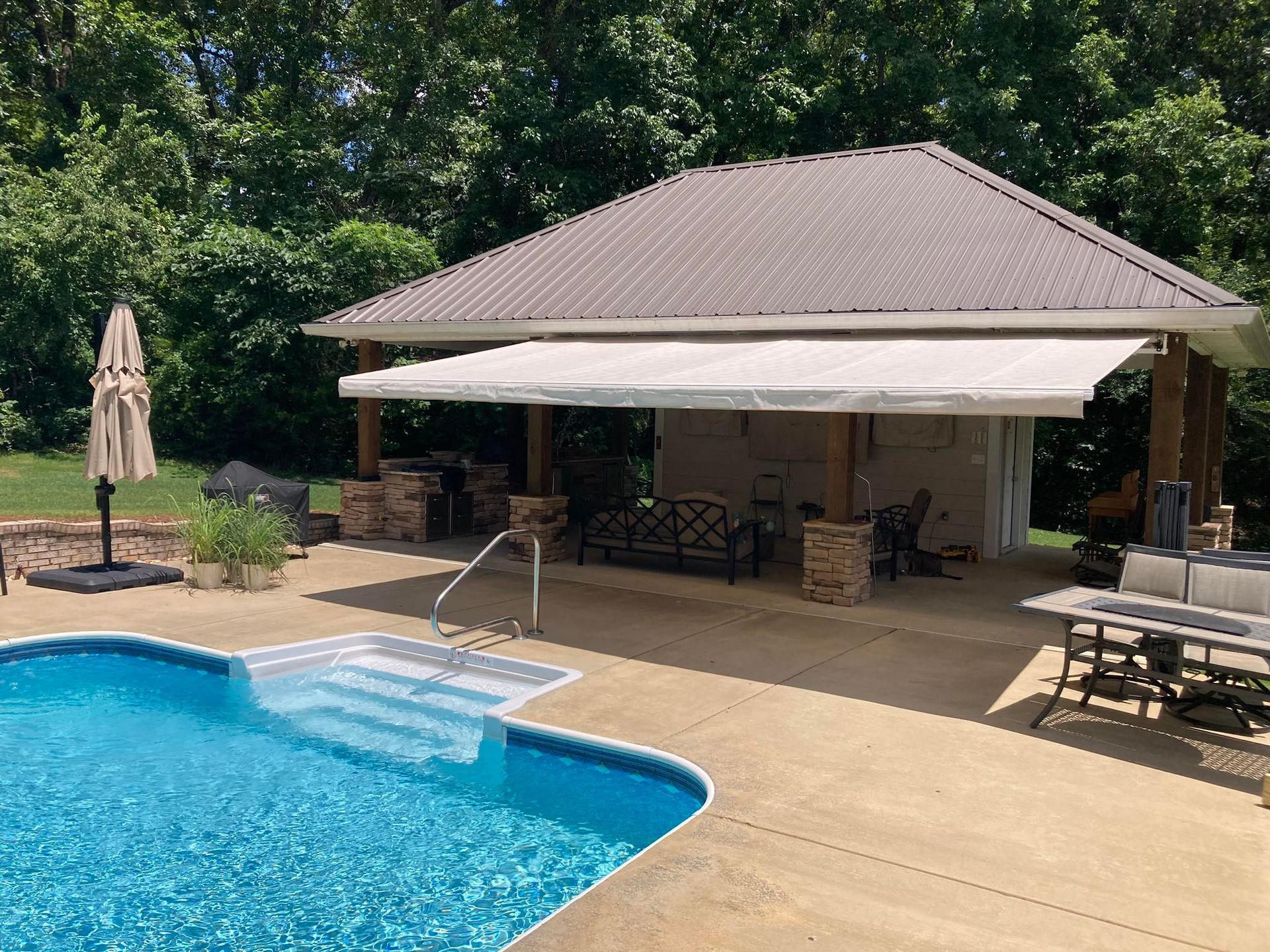 Poolside cabana with an open-air kitchen, awning, and metal roof.