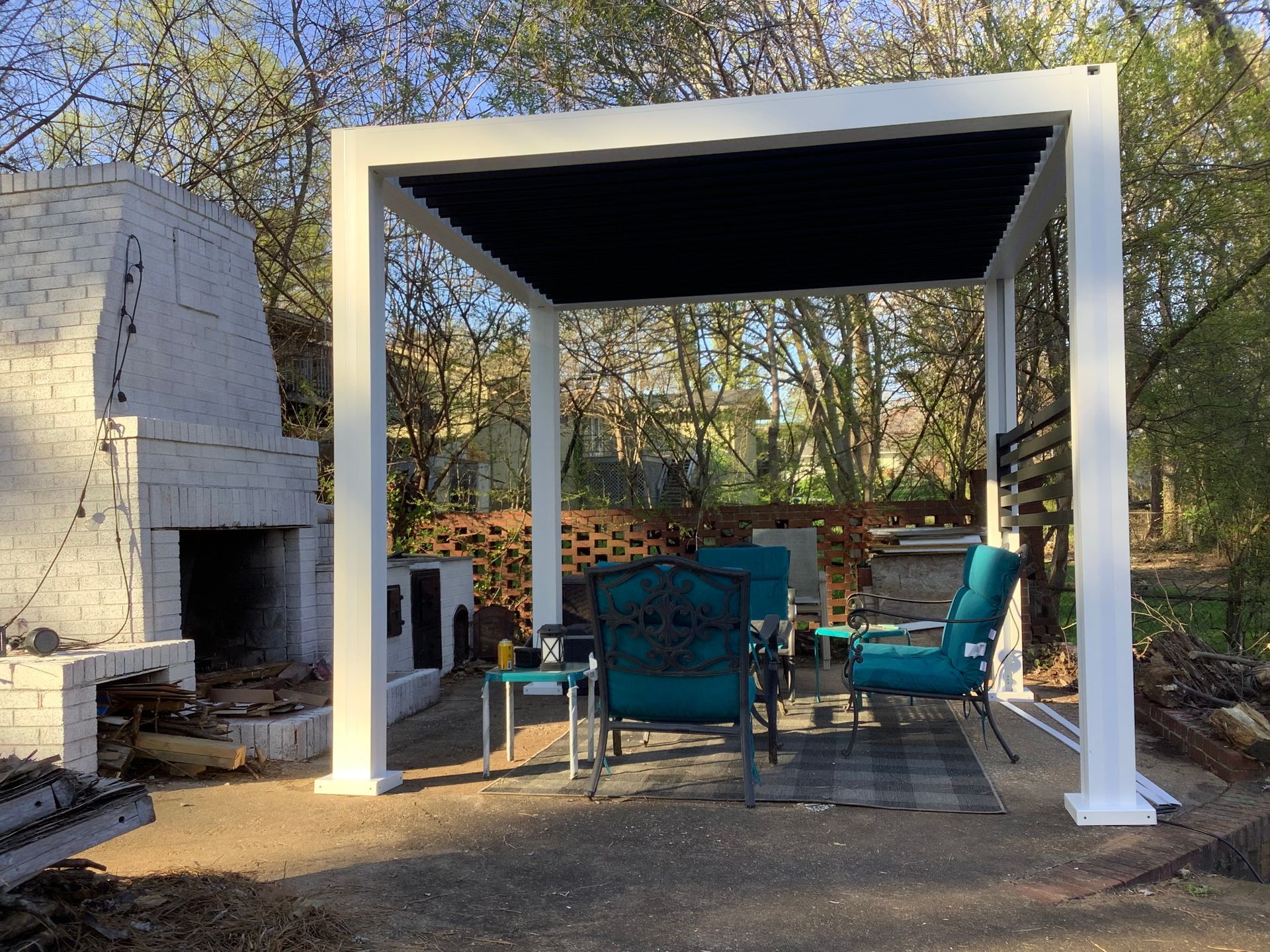 White pergola with dark blue canopy over a patio set. A brick fireplace is to the left.