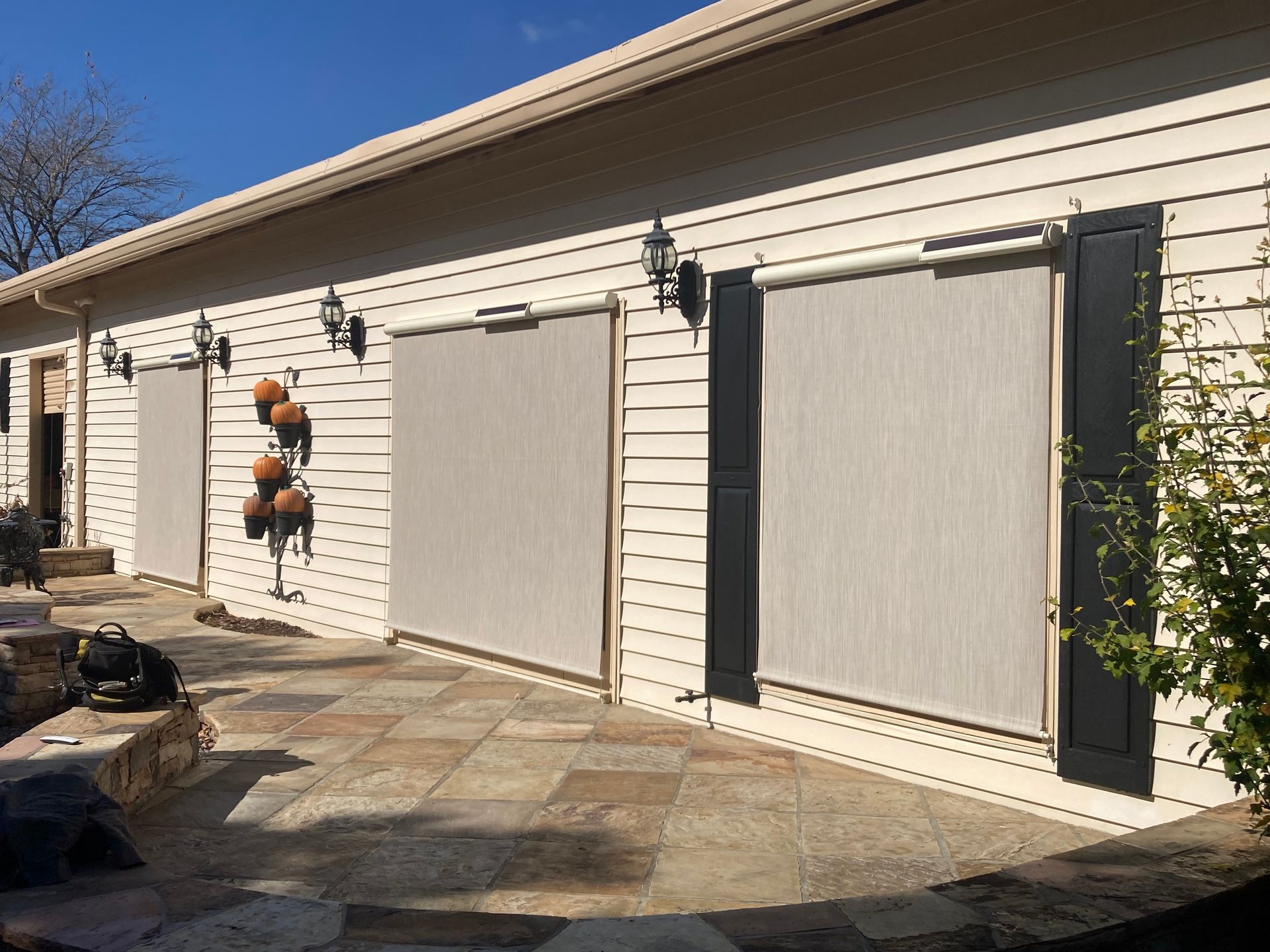 Beige building with three closed outdoor roller shades on a stone patio.