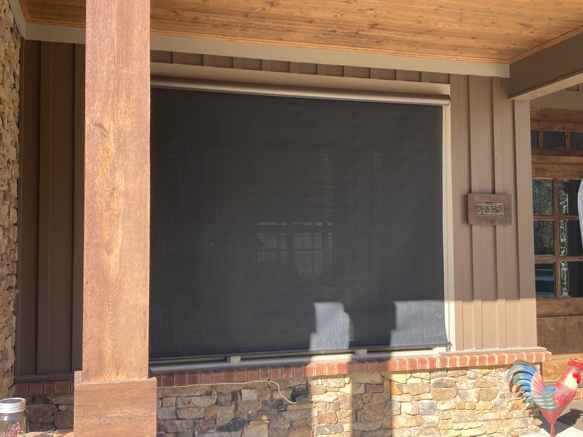 Covered porch with a large, dark screen installed. Wooden post and trim detail the structure.
