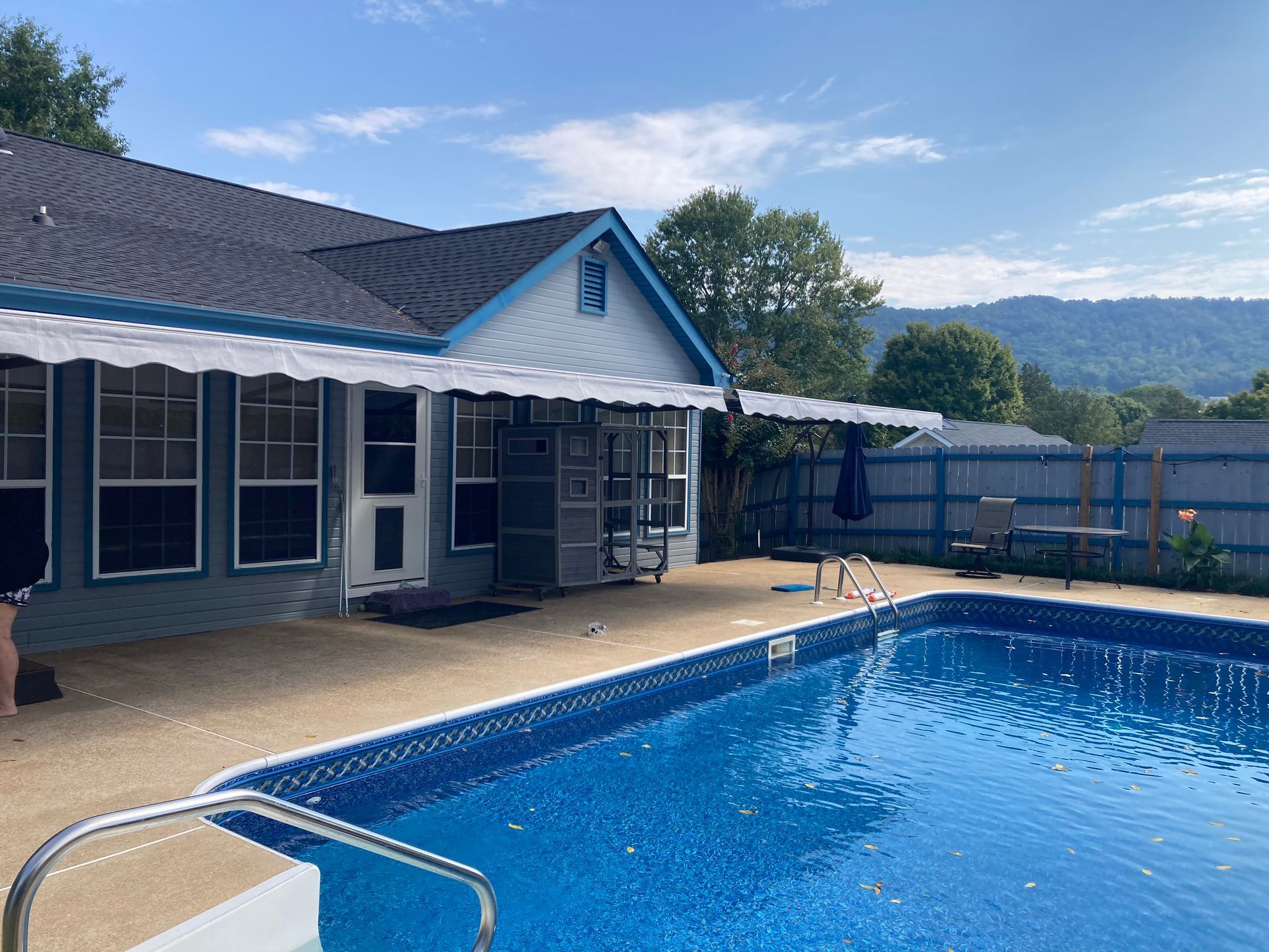 Pool with blue water and house with awning on a sunny day. Mountains in the background.