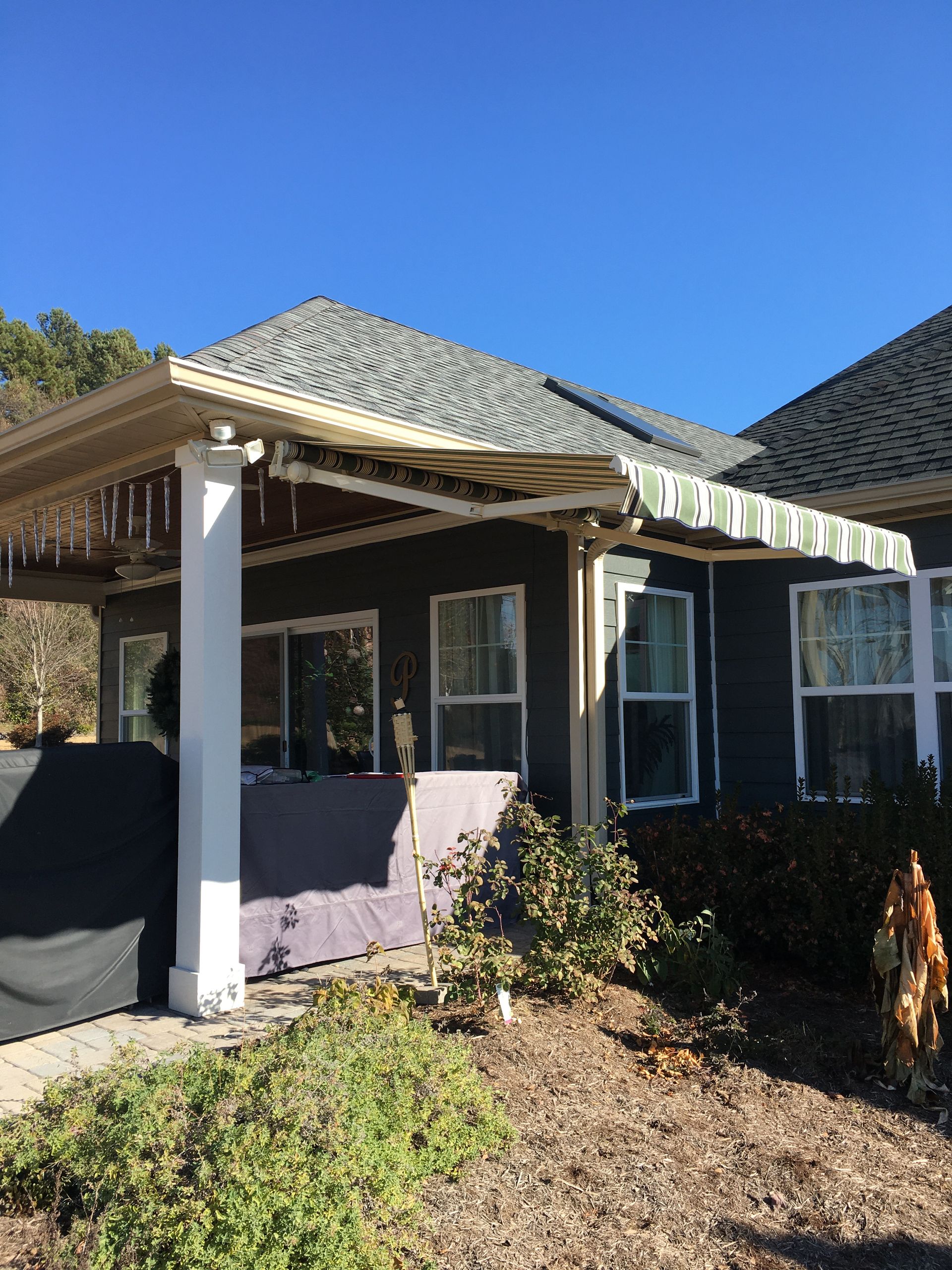 A dark gray house with a striped awning and white columns under a clear blue sky.