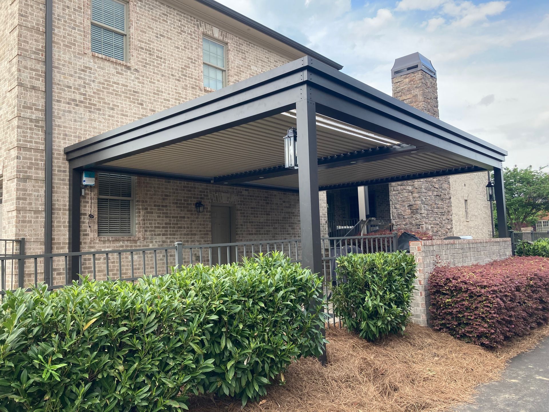 Covered patio with retractable roof, attached to a brick house, overlooking a garden.