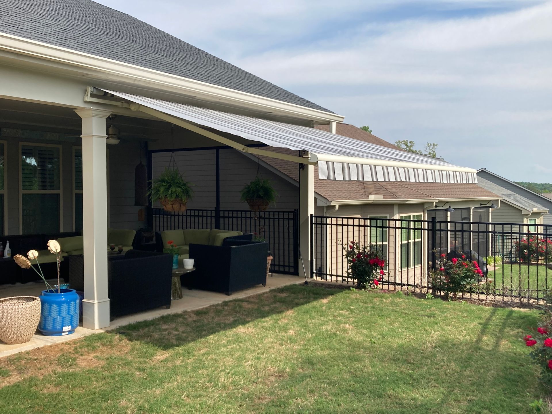 Backyard patio with metal awning, black fence, and green grass.