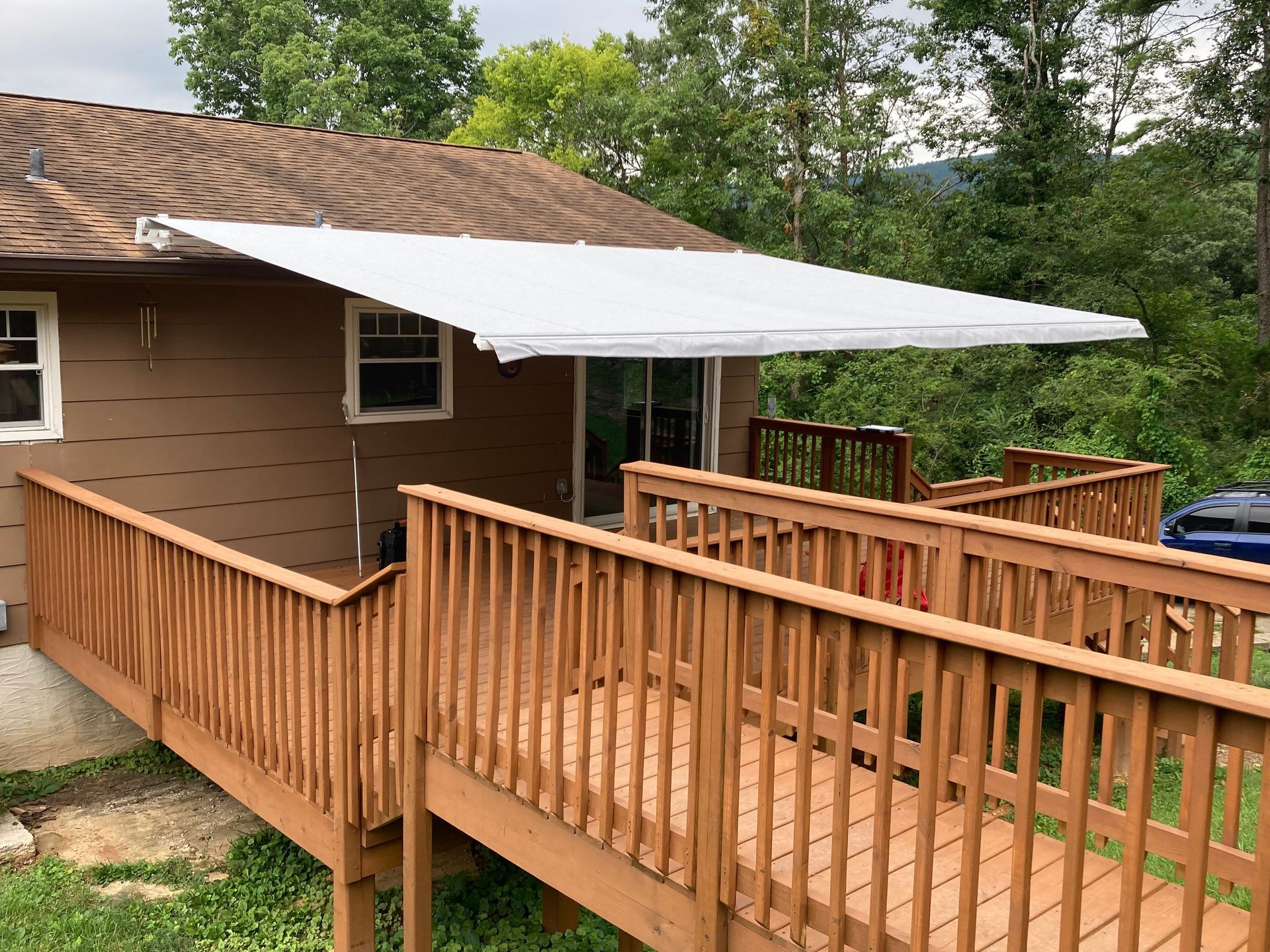 Brown house with white awning over a deck and ramp, trees in background.