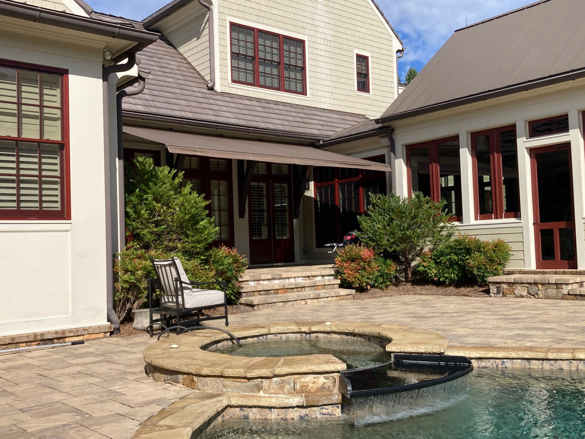 A backyard with a pool, patio, and several connected buildings with brown roofing and trim.
