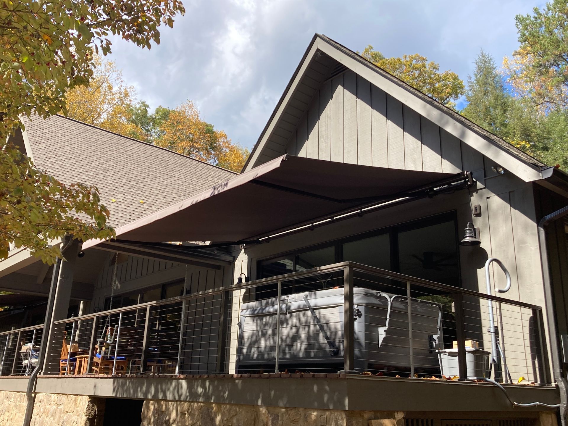Deck of a house with an awning, hot tub, and railing.