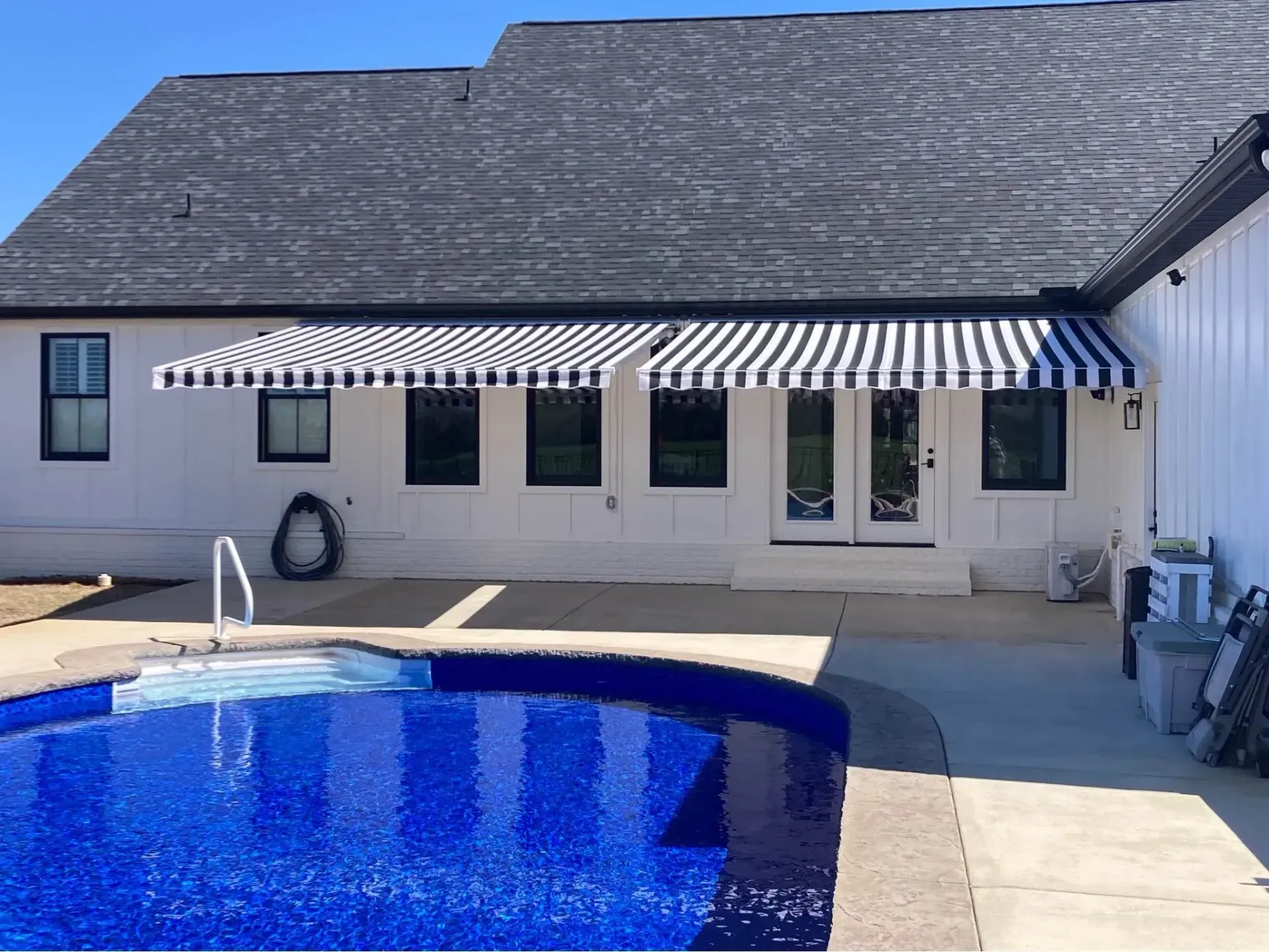 Pool with blue tile and black and white striped awnings on a white house.