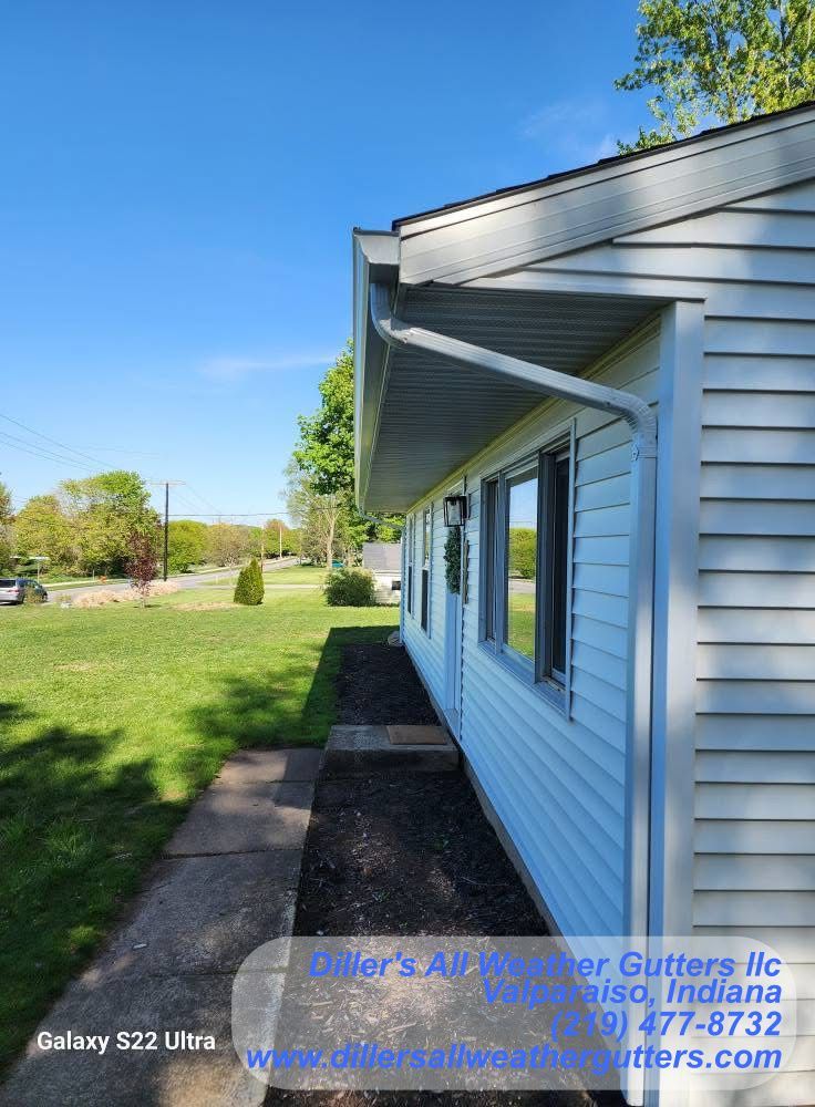 A side view of a house with light blue siding, a white gutter system, and a narrow walkway alongside a dark mulch bed.