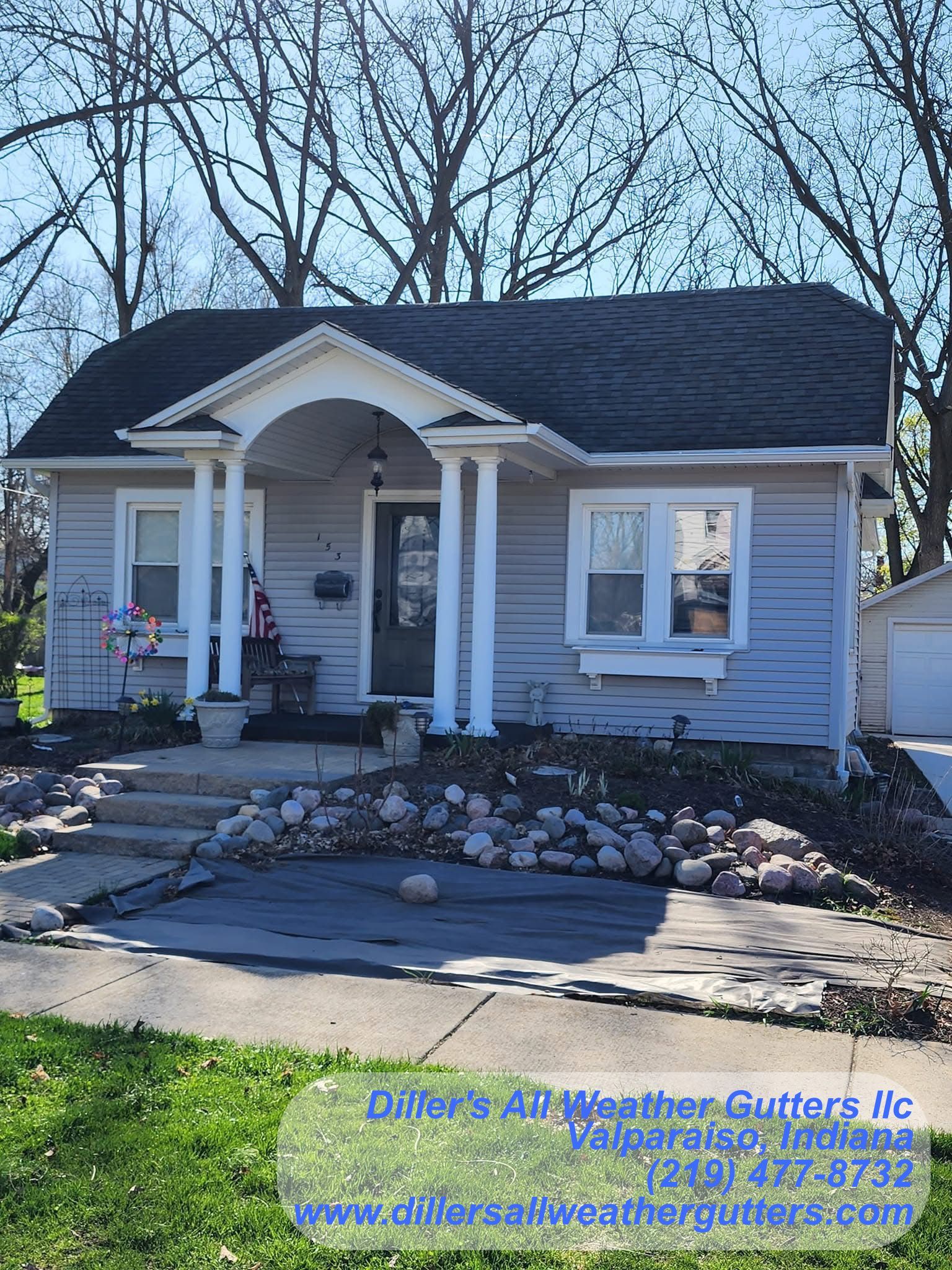 A light gray, single-story house with a white arched front porch, dark roof, and rock landscaping in the front yard.