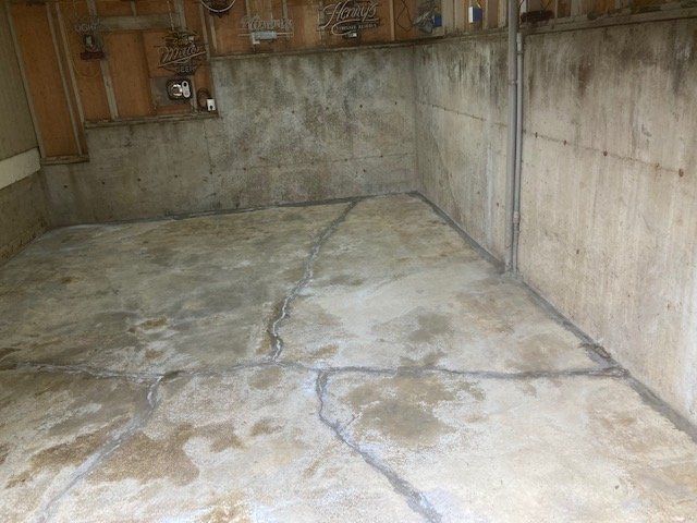 Concrete basement floor with multiple cracks; damp, unfinished walls.