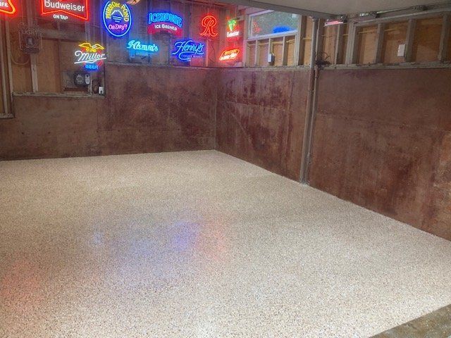 A room with a speckled floor and wooden walls, lit by neon beer signs.