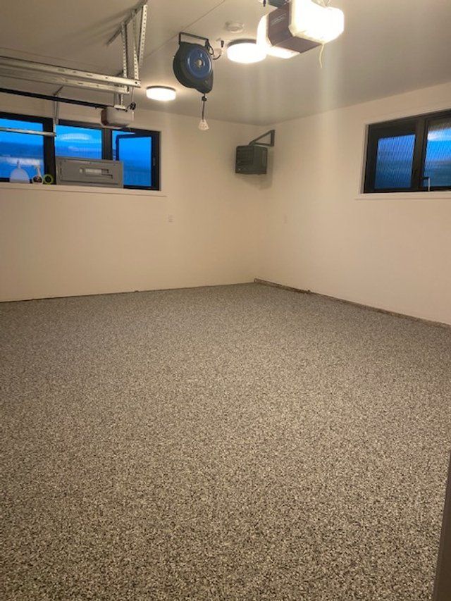 Empty room with speckled flooring, white walls, two small windows, and overhead garage door components.