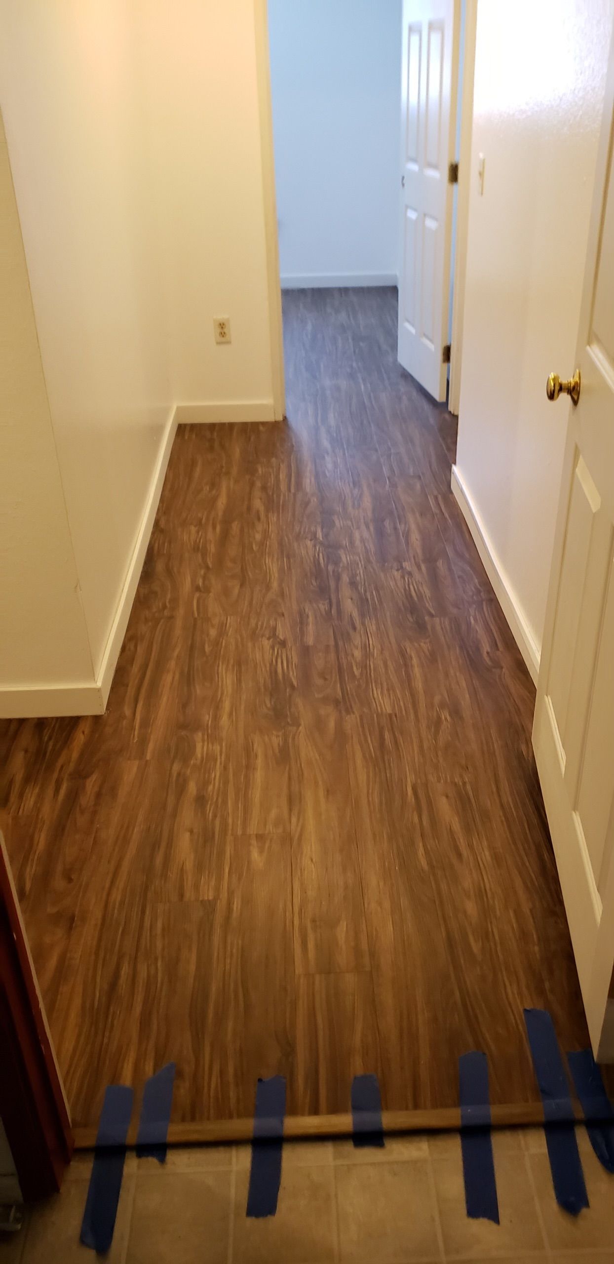 A hallway with a wooden floor and blue tape on the floor.