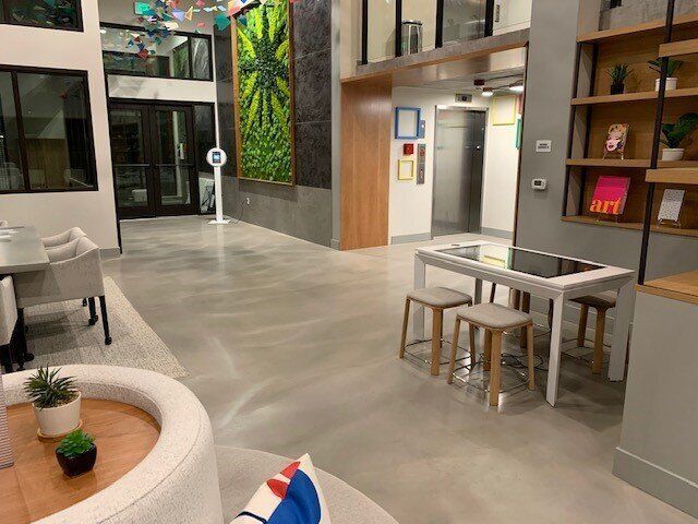 Modern lobby with polished concrete floor, seating area, elevator, and greenery wall.