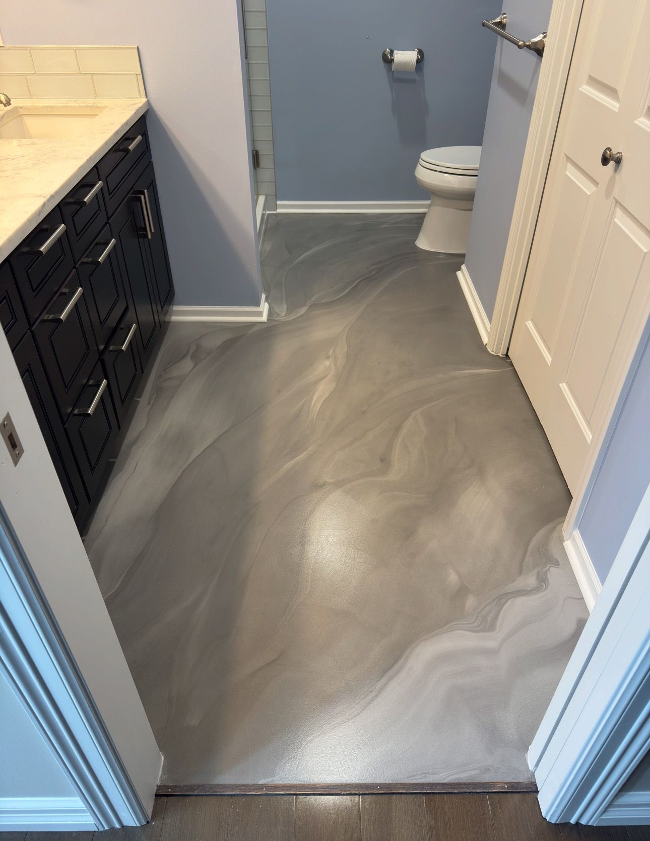 Bathroom with metallic gray epoxy floor, dark blue vanity, white toilet, and blue walls.