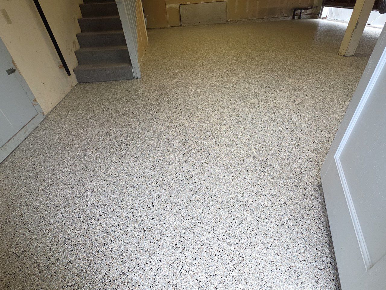 Empty carpeted room with beige speckled flooring and stairs in the background