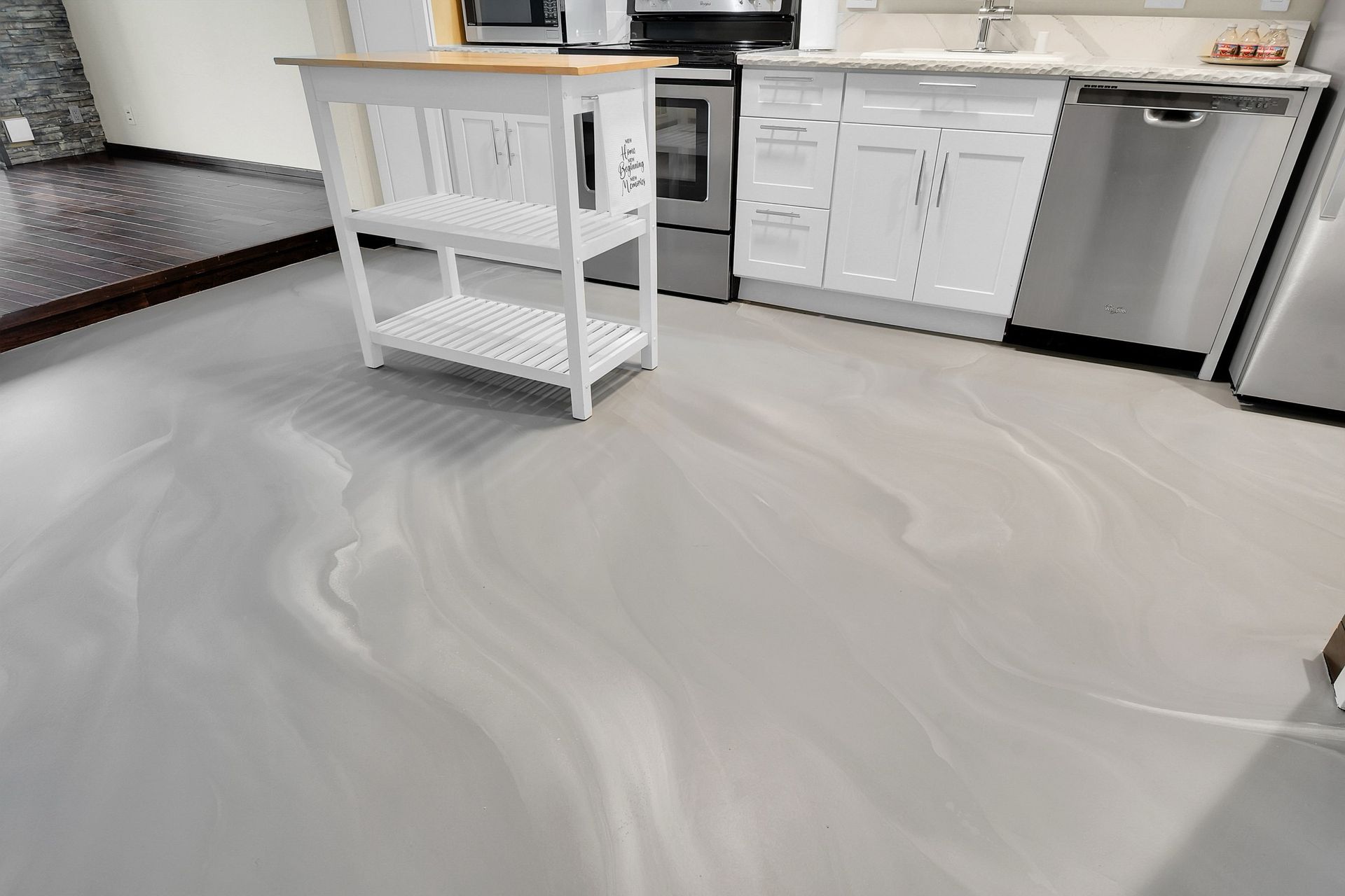 Modern kitchen with white cabinets, stainless dishwasher, and a rolling island on a marbled floor.