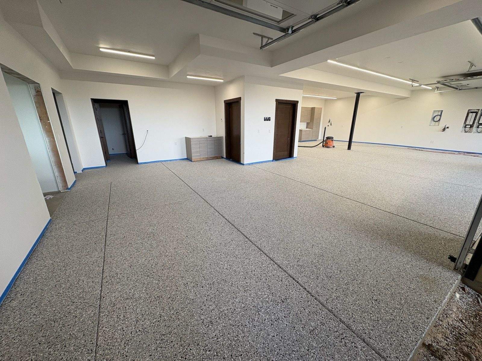 Empty carpeted office room with white walls, ceiling lights, and open doorways
