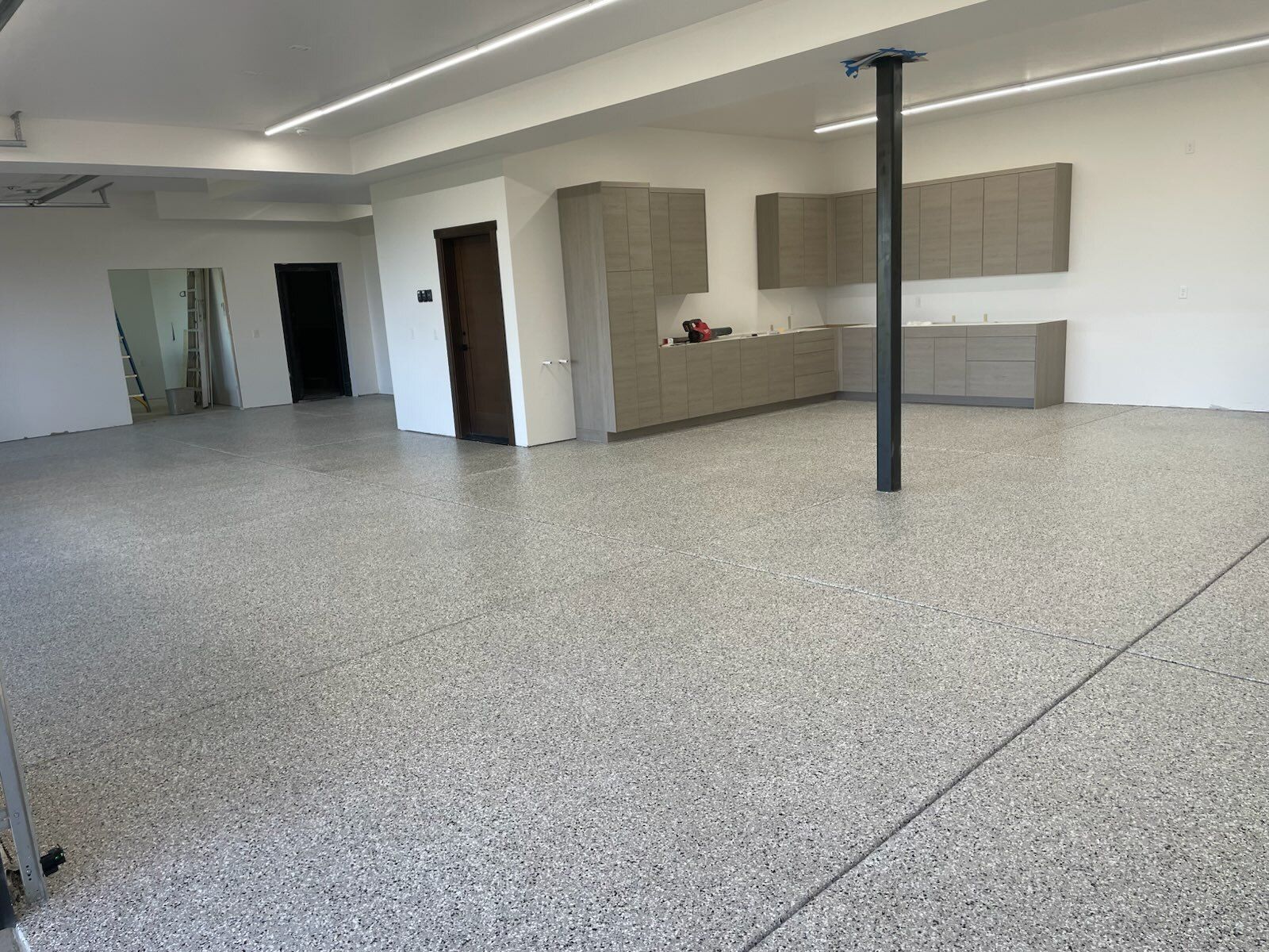 Empty office room with speckled floor, white walls, cabinets, and a black support column.