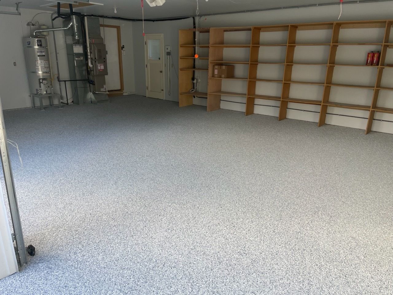 Empty garage with gray speckled floor, shelves along the wall, and water heater equipment in the back.