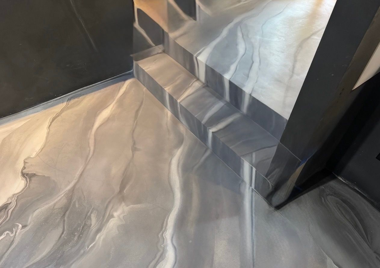 Modern interior corner with gray veined flooring and dark trim beside a sheer curtain