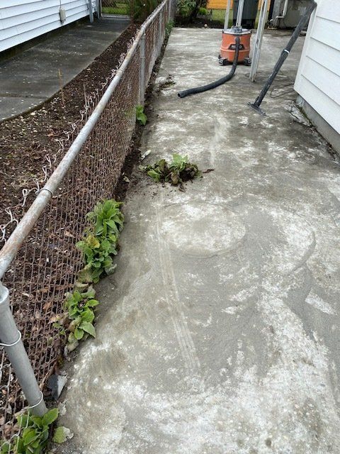 A concrete walkway next to a chain link fence and a vacuum cleaner.