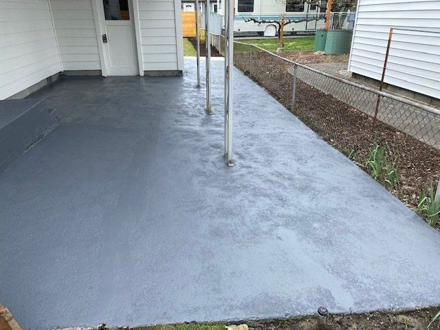 A concrete walkway leading to a house with a fence in the background.