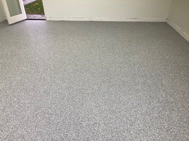 Gray speckled epoxy floor in a room, with white walls and a doorway leading outside.