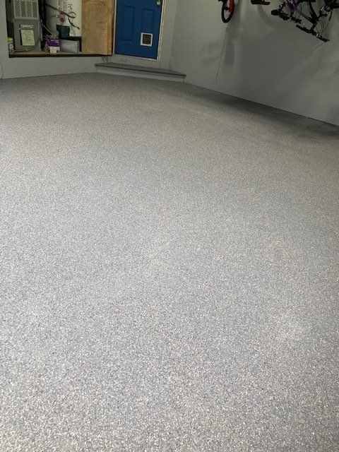 Garage with light gray speckled epoxy floor. Blue door with pet door. Bicycle hanging on wall.