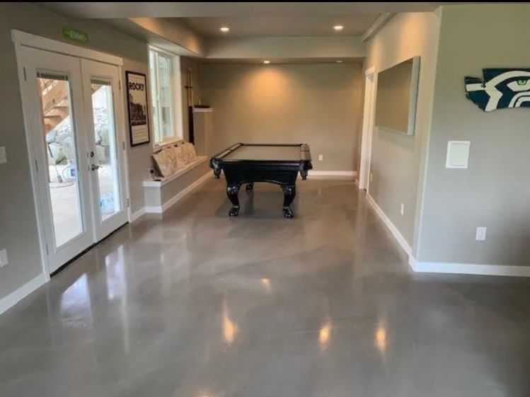 A gray-floored rec room with a pool table, double doors, and a Seahawks logo on the wall.