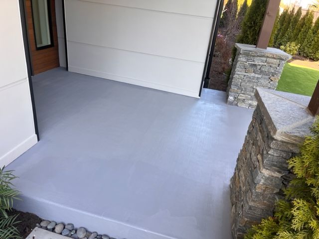 A concrete porch next to a garage door and a stone wall.