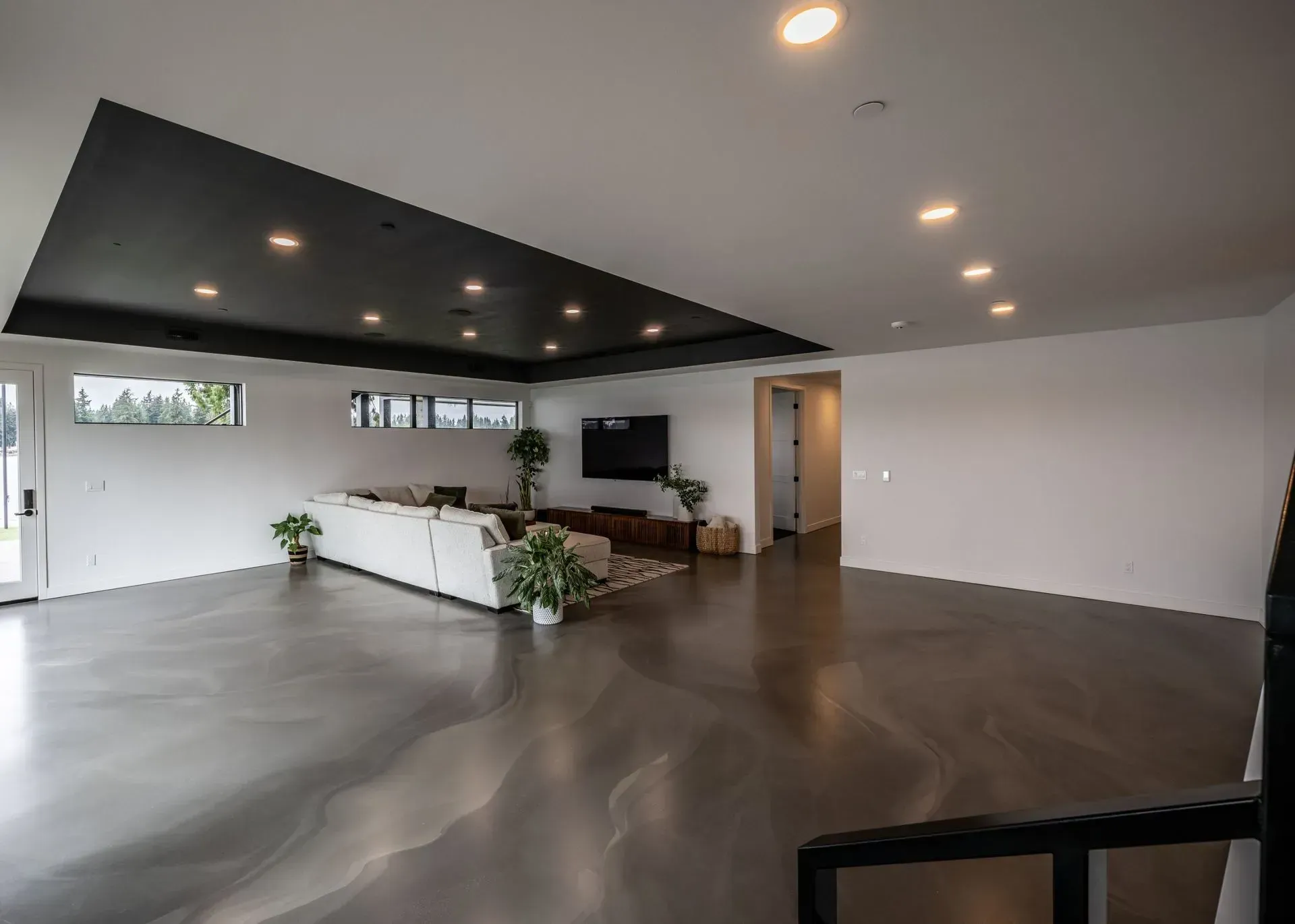 Spacious modern living room with gray floors, white walls, black ceiling, sectional sofa, and a TV.
