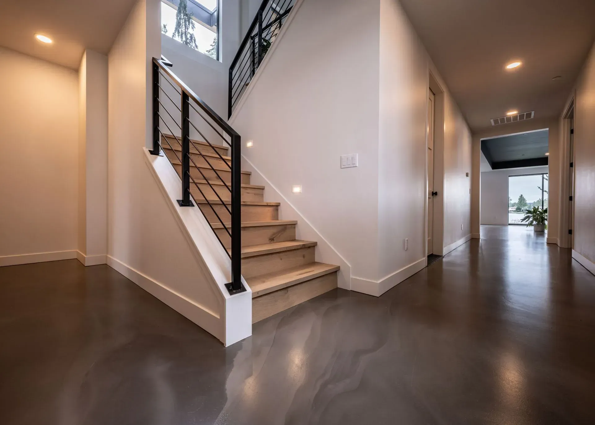Hallway with stairs and polished concrete floor. White walls, black railing, and recessed lighting.