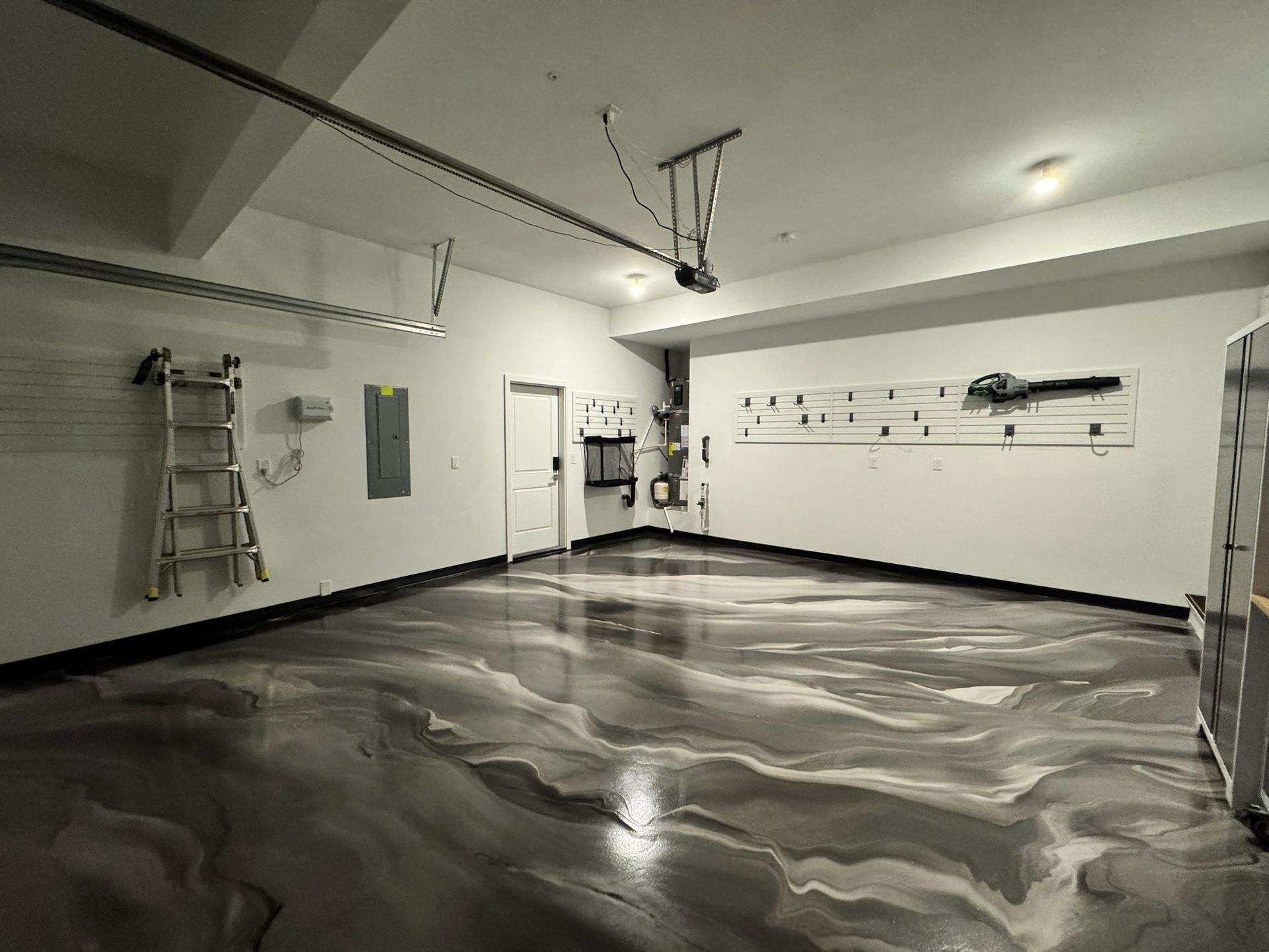Garage interior with glossy gray and white epoxy floor, white walls, and a garage door opener.
