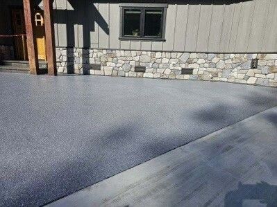 Exterior view of a house with a gray epoxy-coated driveway, stone foundation, and light gray siding.