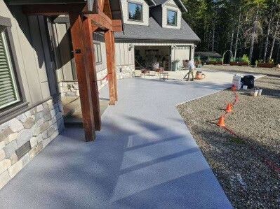 Exterior view of a house with a gray concrete driveway and walkway. Sunlit, with wooden porch supports and a garage.
