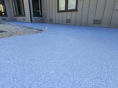 Blue concrete patio next to a house with beige siding, light gravel border.
