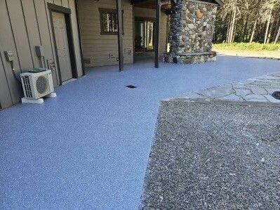 Blue speckled concrete patio next to a gravel area and a building with a stone chimney.