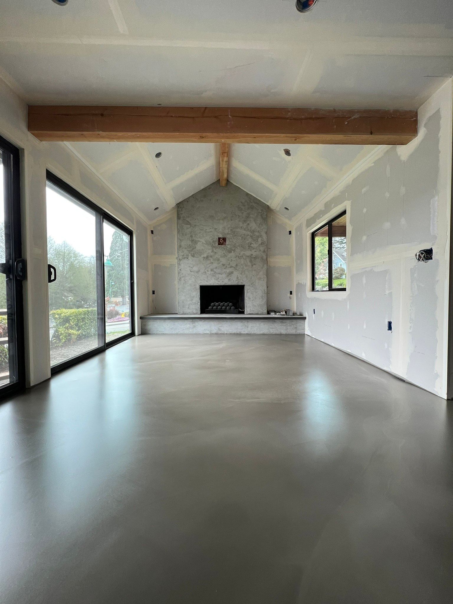 Spacious room under construction, with concrete floor, fireplace, and exposed wood beam.