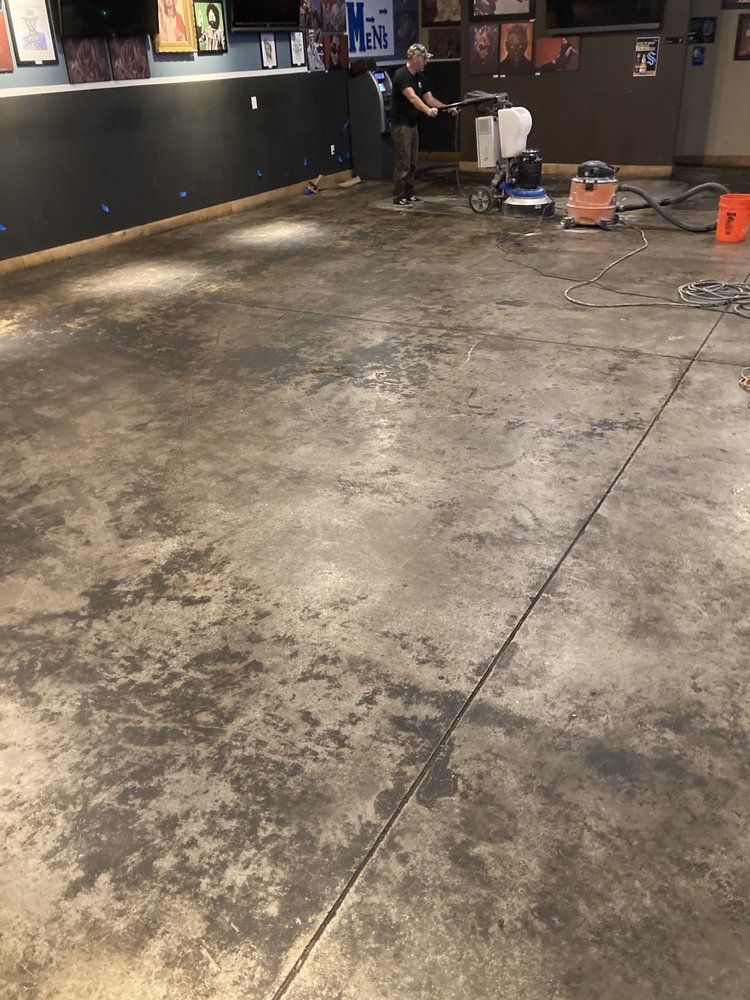 A man is cleaning a dirty concrete floor in a room.