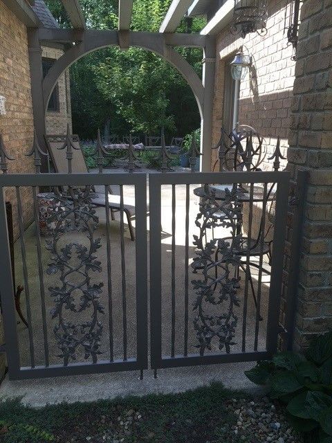 Ornate black metal gate in a stone courtyard, with an arched opening and greenery beyond